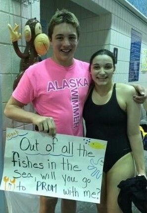 two people standing next to each other holding a sign that says out of all the fishes in the sea will you go to prom with me?