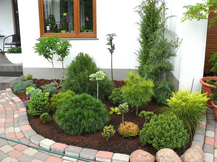 a garden area with plants and rocks in front of a white house on a cobblestone walkway