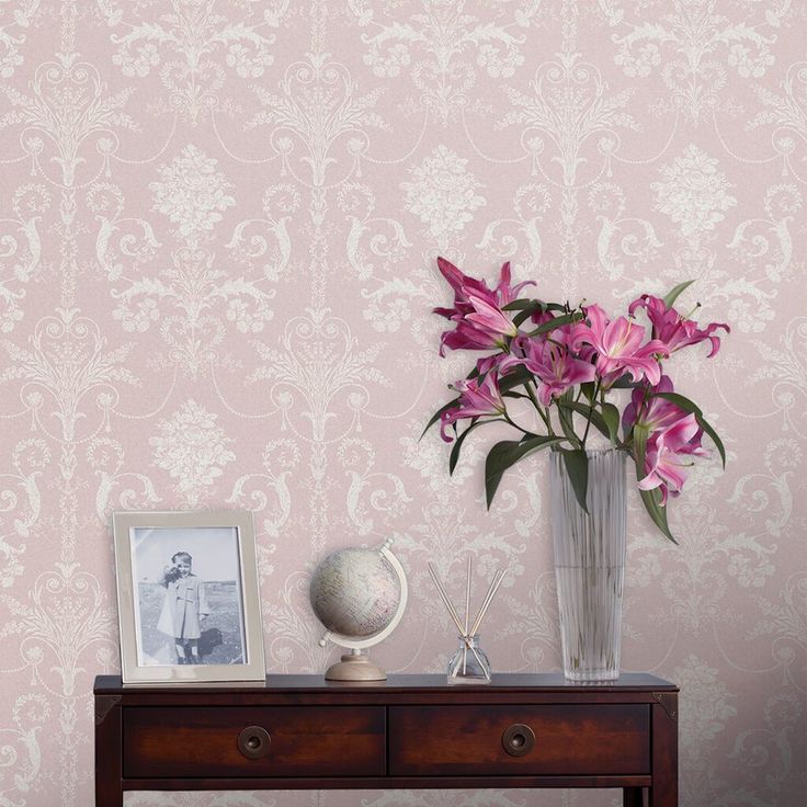 a vase with pink flowers on a table next to a wallpapered wall behind it