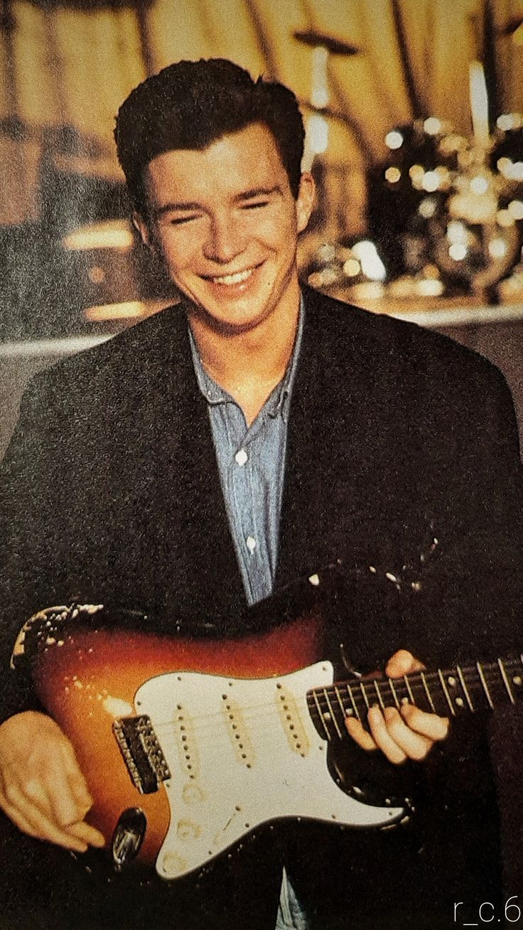 a young man smiles while playing an electric guitar