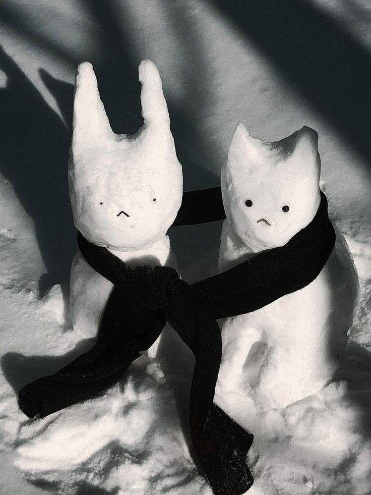 two small stuffed animals wearing black ties on a white surface with shadows from the fabric