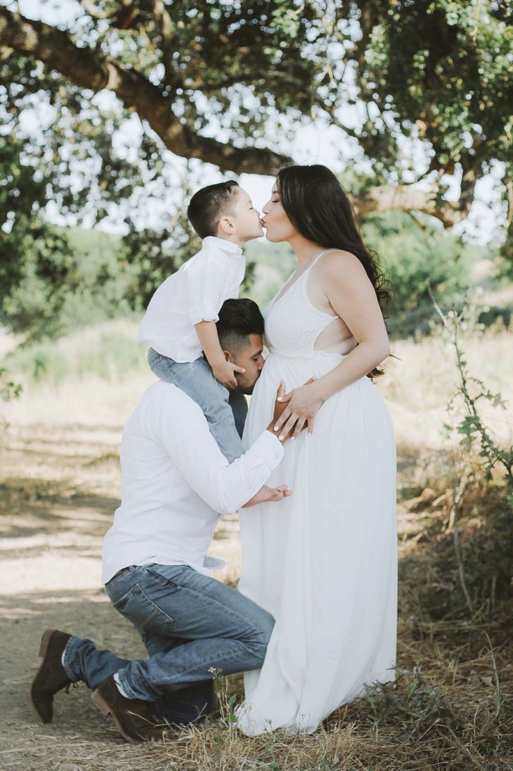 a man kneeling down to kiss his pregnant wife's belly as she kisses her husband