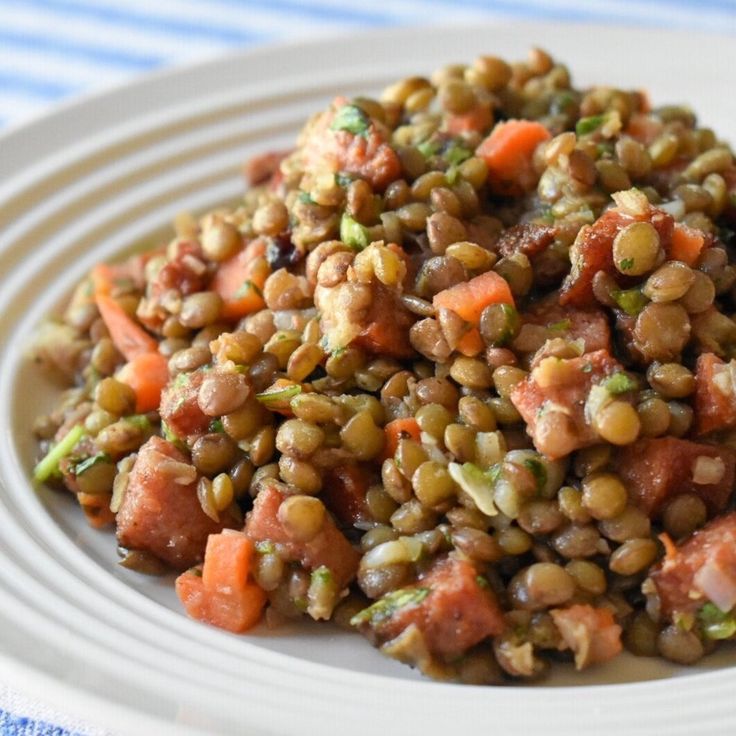 a white plate topped with lentils and carrots on top of a blue and white table cloth