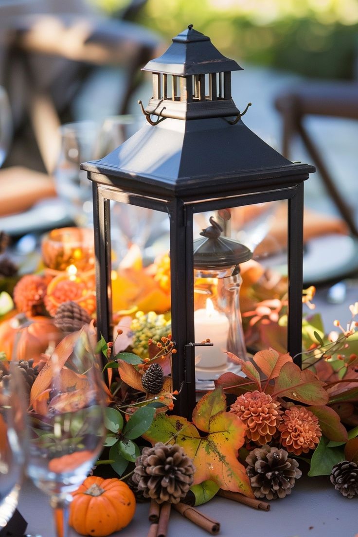 a lantern on top of a table filled with flowers and pineconis, surrounded by wine glasses