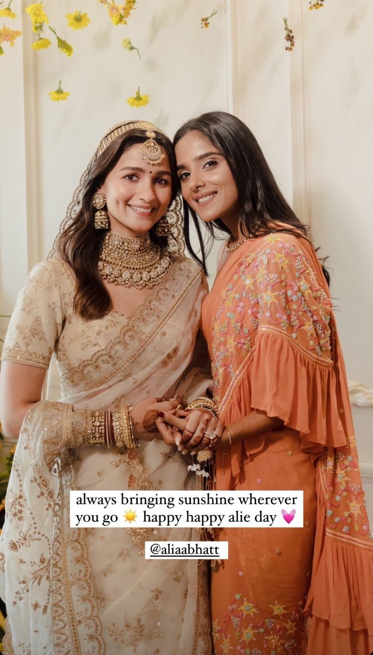 two women standing next to each other in front of a wall with flowers on it