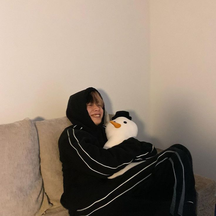 a person sitting on a couch wrapped in a blanket and holding a stuffed animal penguin