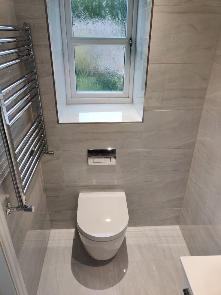 a white toilet sitting next to a window in a bathroom under a window sill