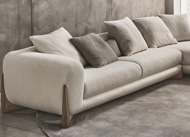 a couch with many pillows on it in front of a concrete wall and rugs