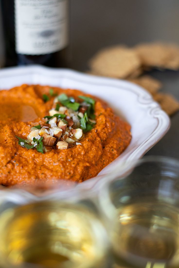 a white plate topped with hummus next to crackers and a bottle of wine