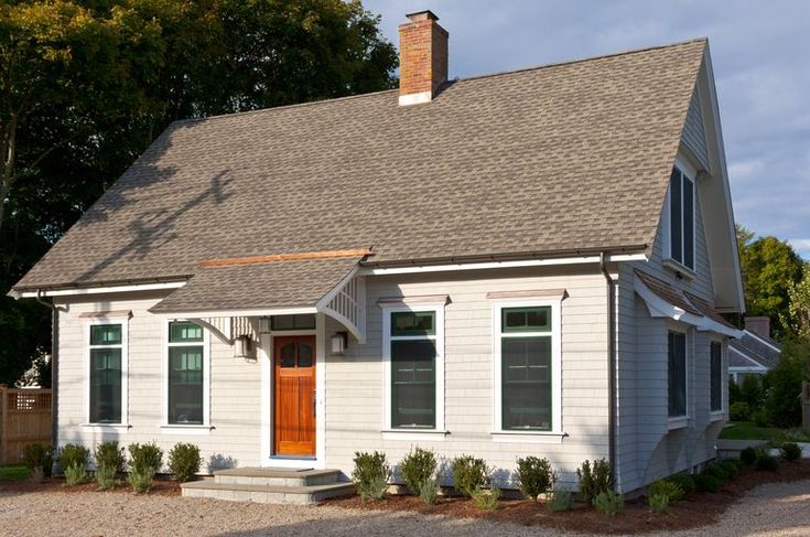 a small white house with a red door and brown shutters on the front porch