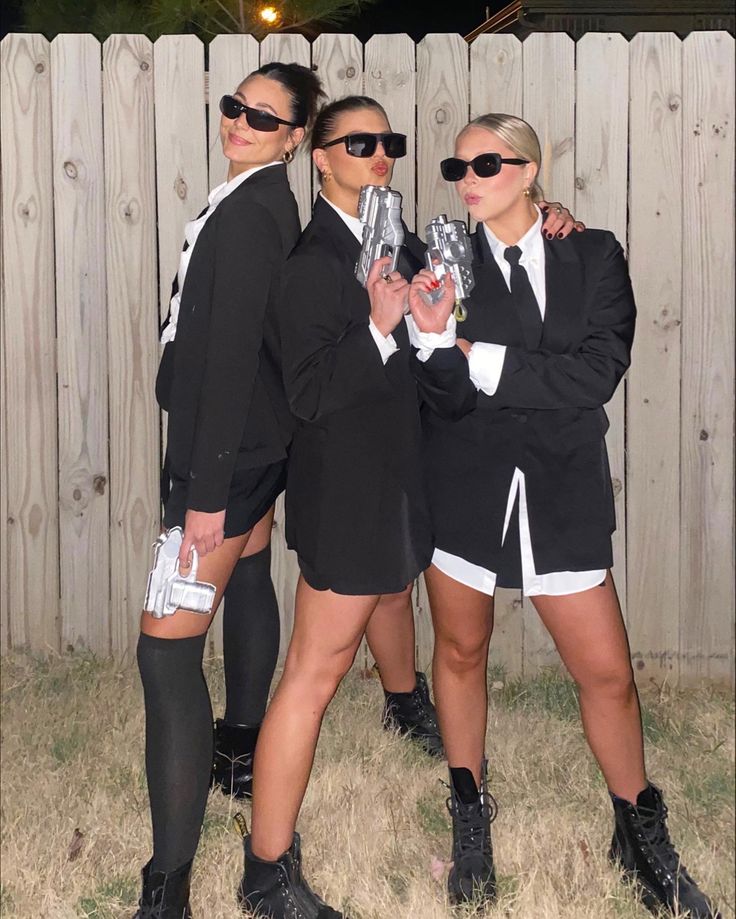 three women dressed in black and white posing for the camera with one holding a silver object