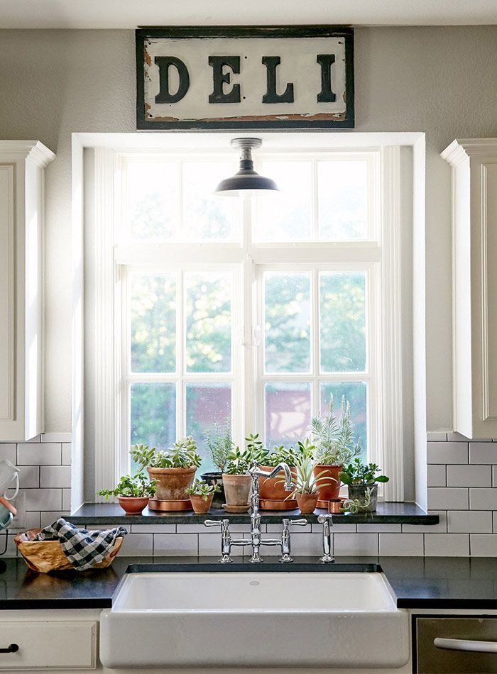 a kitchen sink sitting under a window with potted plants on top of the counter