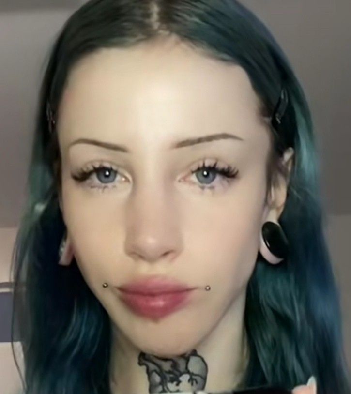 a woman with blue hair and piercings on her neck is looking at the camera