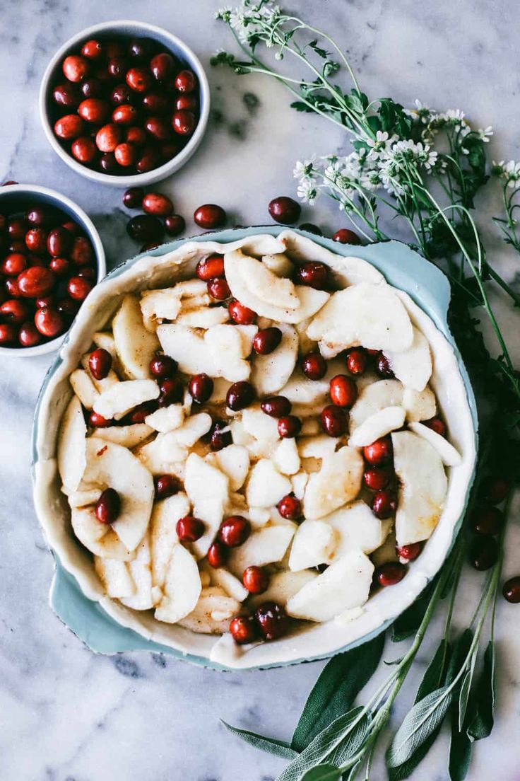 apples and cranberries are in bowls on a marble surface with greenery around them