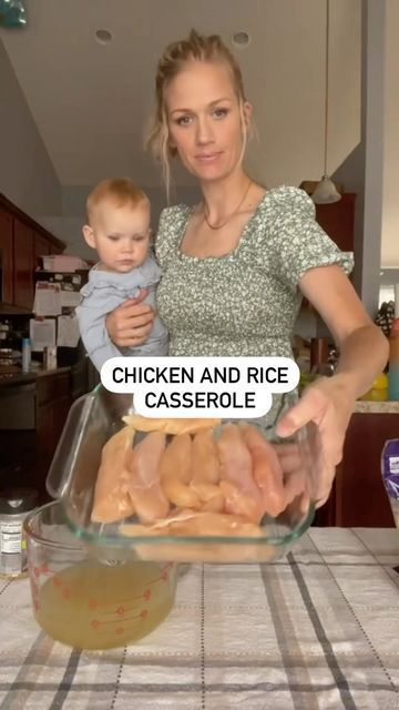 a woman holding a baby in front of a glass bowl filled with chicken and rice casserole