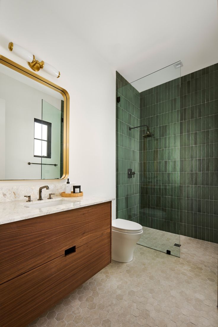 a bathroom with green tiled walls and a wooden vanity, mirror, and shower stall