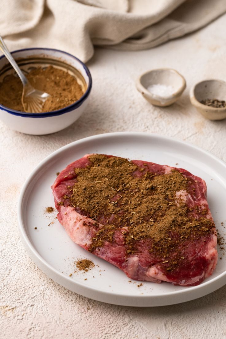 a piece of steak on a plate with spices and seasoning next to the meat