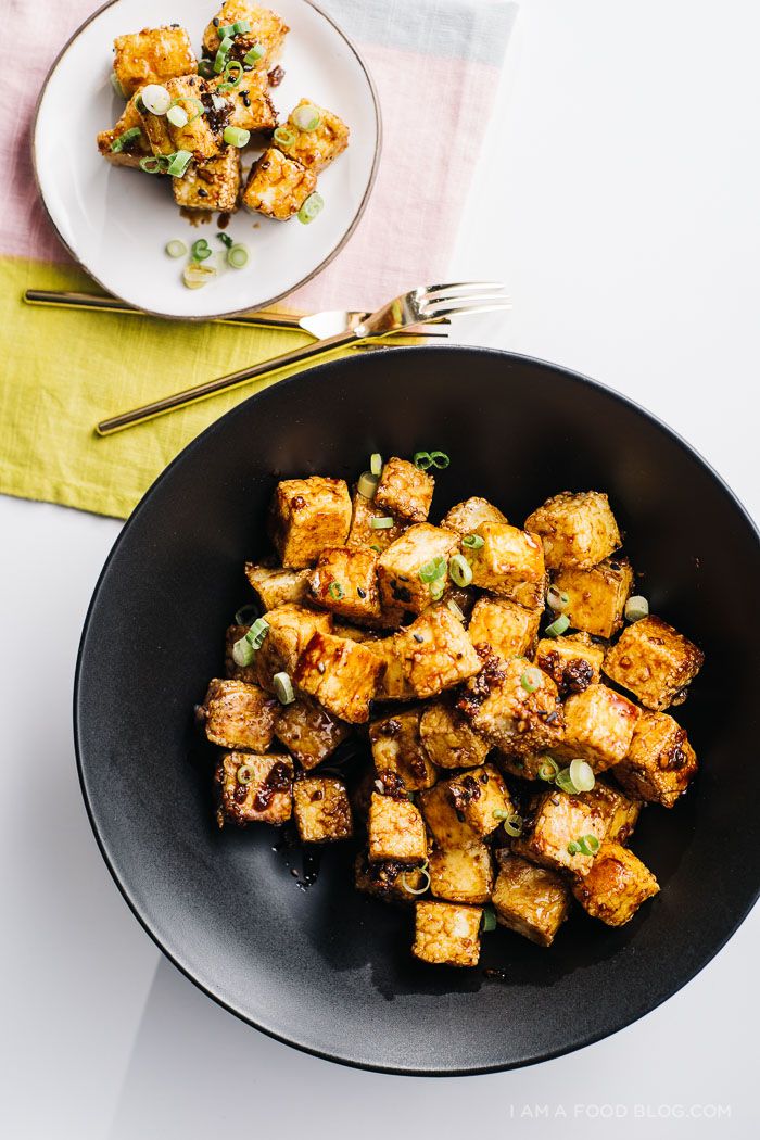 a black bowl filled with fried tofu next to a fork and knife on a white table