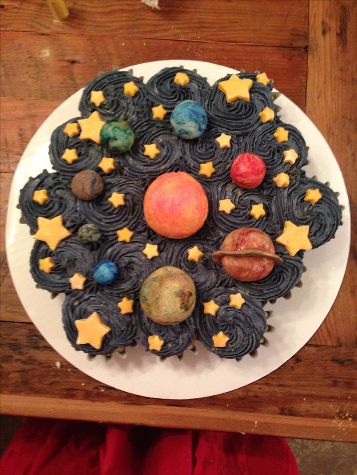 a space themed cake on a white plate with stars and planets around it, sitting on a wooden table