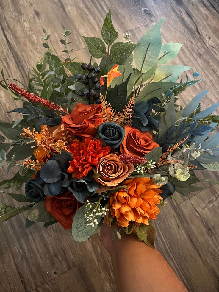 a hand holding a bouquet of flowers on top of a wooden floor