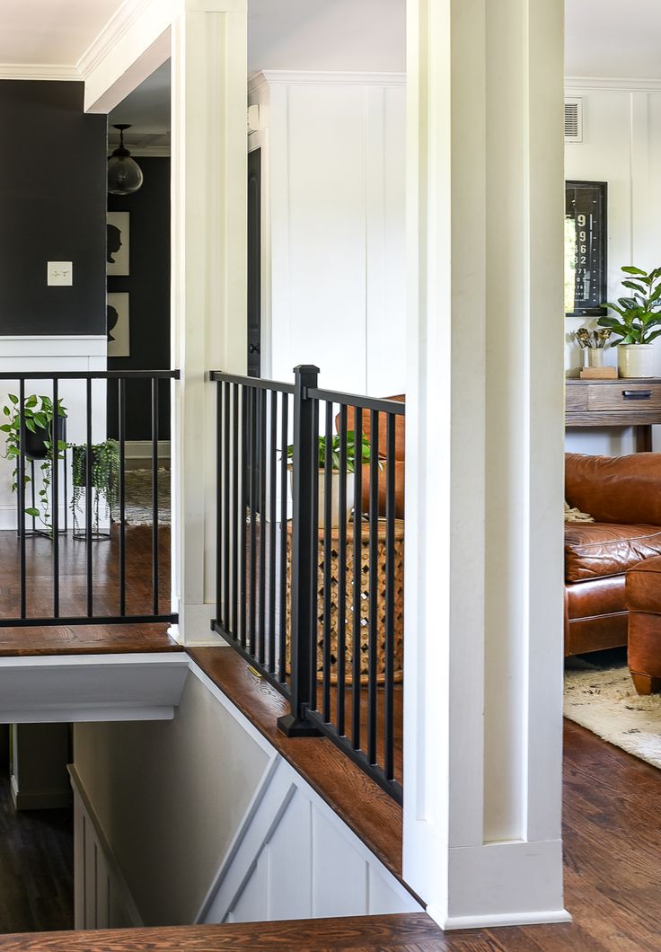 a living room filled with furniture next to a wooden floor and white walls in front of a staircase