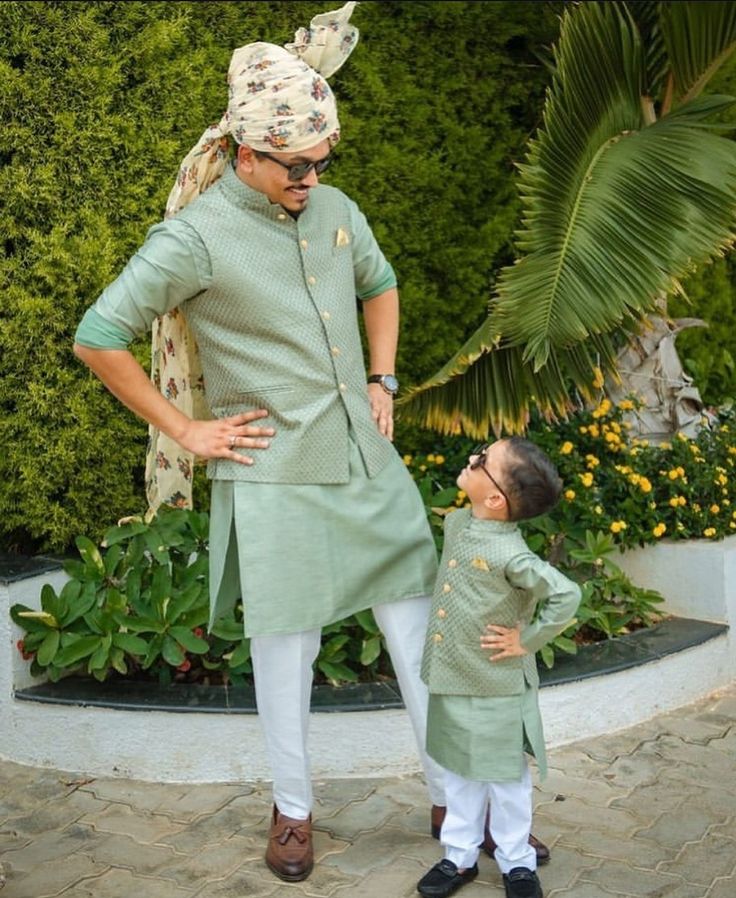 a man standing next to a little boy wearing a green shirt and white pants with his hands on his hips