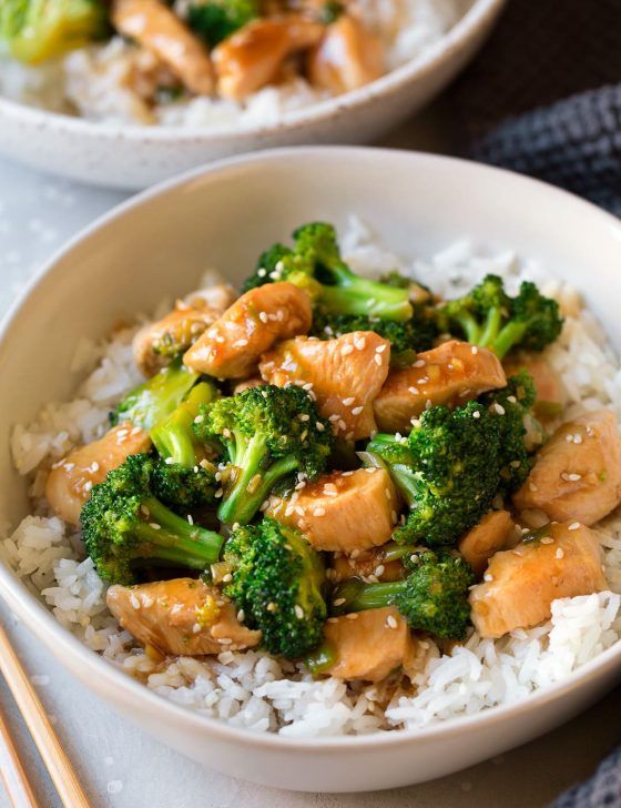 two bowls filled with chicken and broccoli on top of white rice next to chopsticks