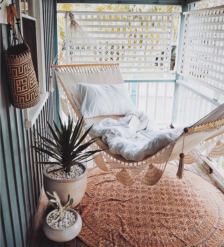 a hammock is sitting on the porch with pillows and plants next to it