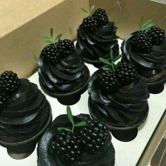 black cupcakes with chocolate frosting and berries on top are arranged in a box