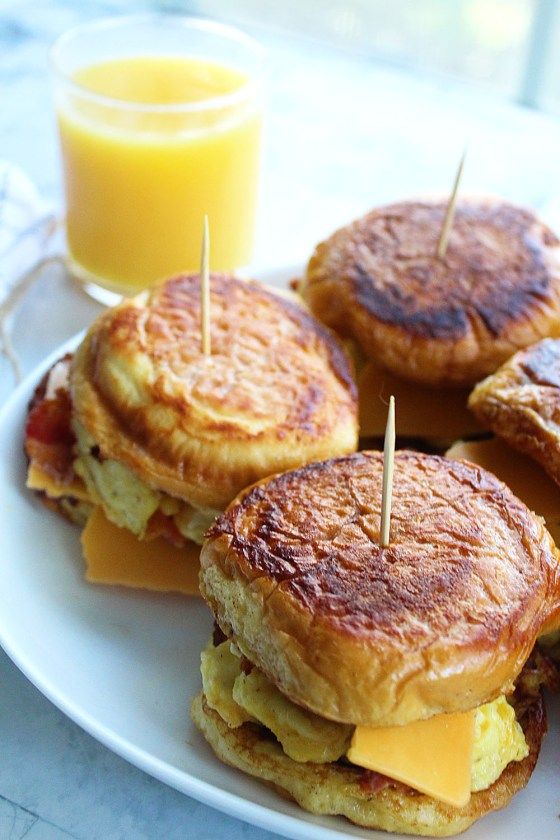 three breakfast sandwiches on a white plate with orange juice