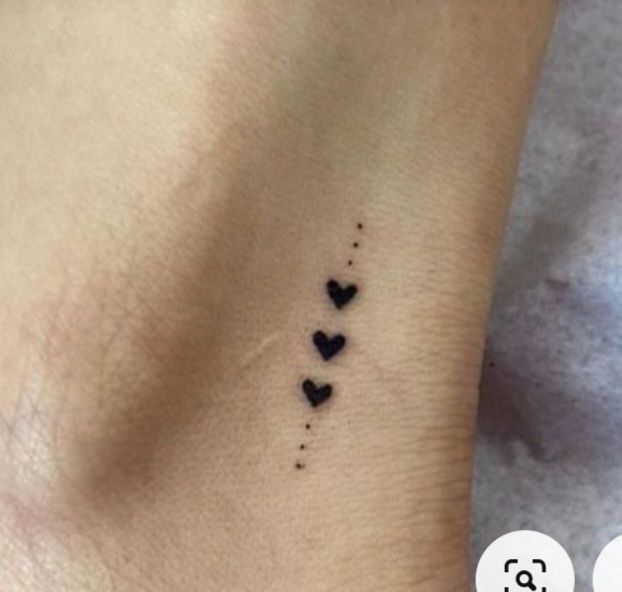 a small black heart tattoo on the side of a woman's left arm and foot