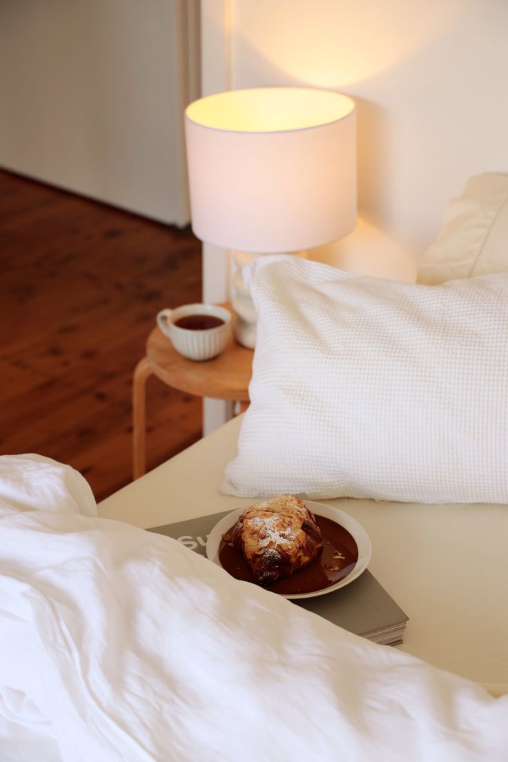 a plate of food sitting on top of a bed next to a night stand and lamp