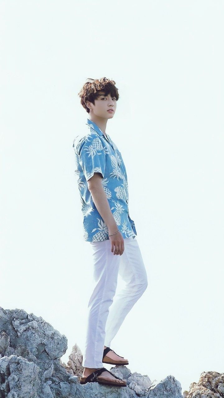 a young man standing on top of a rocky hill wearing white pants and a blue shirt