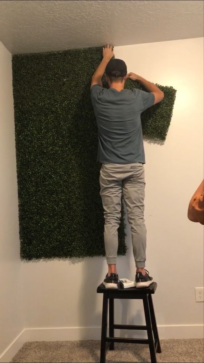 a man standing on top of a stool in front of a fake grass plant wall