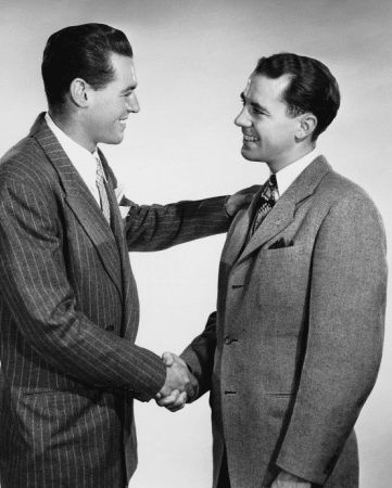 two men in suits shaking hands with each other on a gray and white background stock photo