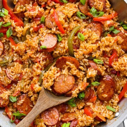 a skillet filled with rice, sausage and peppers