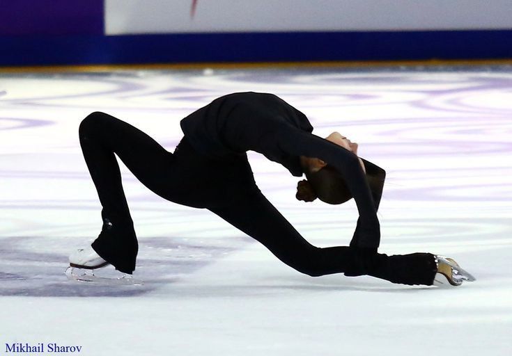 a man skating on an ice rink wearing a black suit and white shoes with his hands in the air