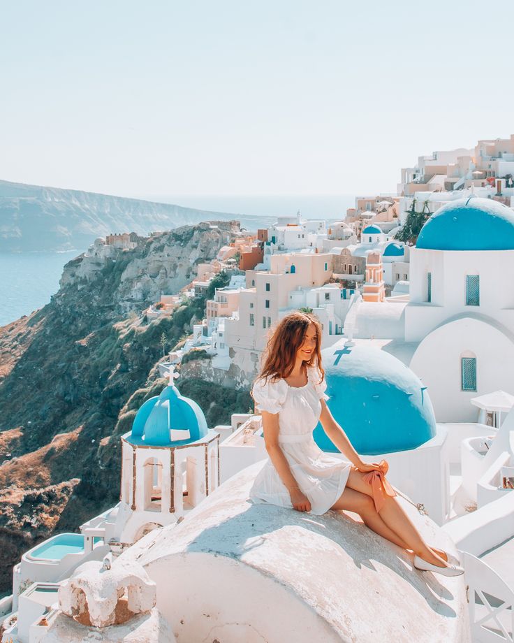 a woman sitting on top of a white building next to the ocean with blue domes