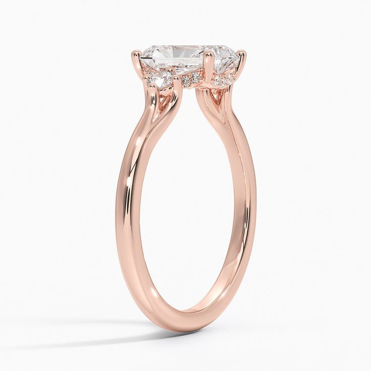 Radiant Cut Floating Three Stone Diamond Engagement Ring - 14K Rose Gold. A classic three stone ring silhouette is updated by a unique open gallery, allowing maximum light to reach the floating diamond. A hidden halo of diamonds wraps the gallery wire in shining light (1/6 total carat weight). Luxury Rose Gold Emerald Cut Ring, Luxury 14k Rose Gold Wedding Ring With Center Stone, Rose Gold Princess Cut Diamond Ring With Vvs Clarity, Princess Cut Rose Gold Ring With Vvs Clarity, Classic Three Stone Rose Gold Jewelry, Classic Three-stone Rose Gold Jewelry, Rose Gold Solitaire Asscher Cut Jewelry, Timeless Rose Gold Round Cut Diamond Ring, Formal 14k Rose Gold Ring With Prong Setting