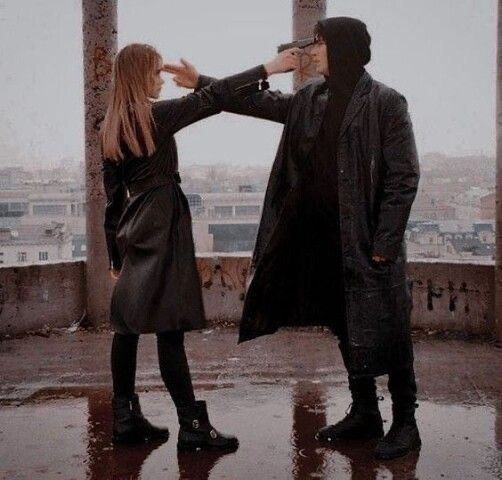 a man and woman standing on top of a roof next to each other in the rain