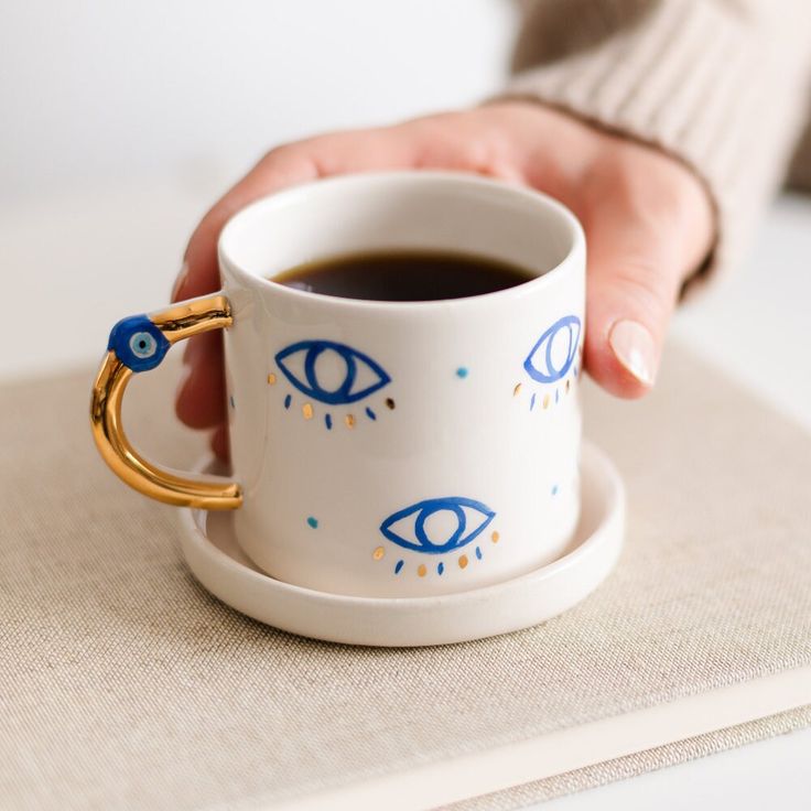 a person holding a coffee cup with an eye design on it and a gold ring