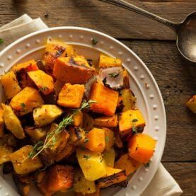 a white plate topped with roasted potatoes on top of a wooden table next to a spoon