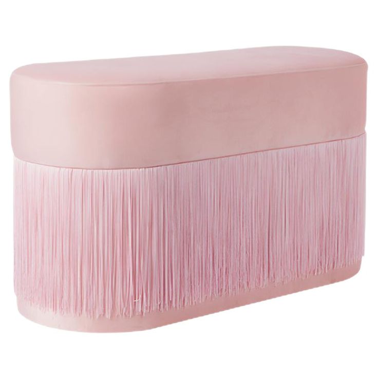 a pink ottoman with fringes on the top and bottom, sitting in front of a white background