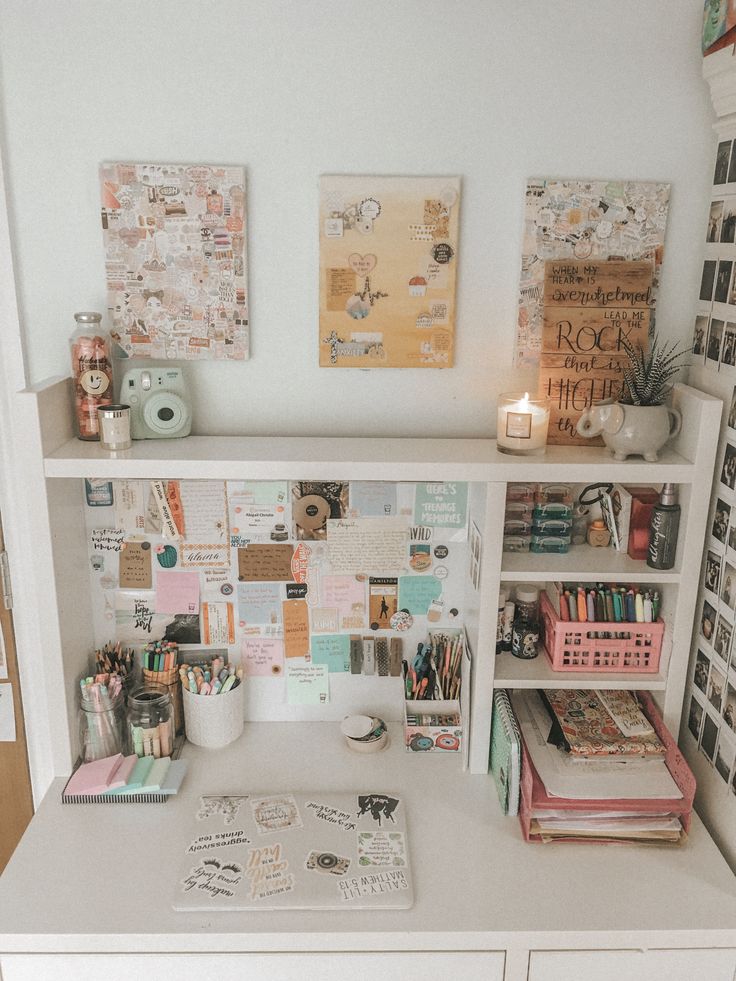 a white desk topped with lots of clutter and books next to a wall covered in pictures