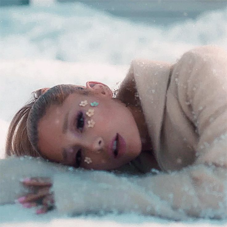 a woman laying in the snow with her eyes closed and nose piercings on top of her head