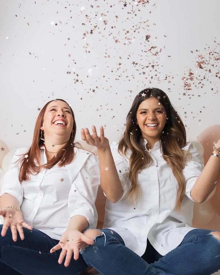 two women sitting on the floor with confetti falling from their mouths and hands