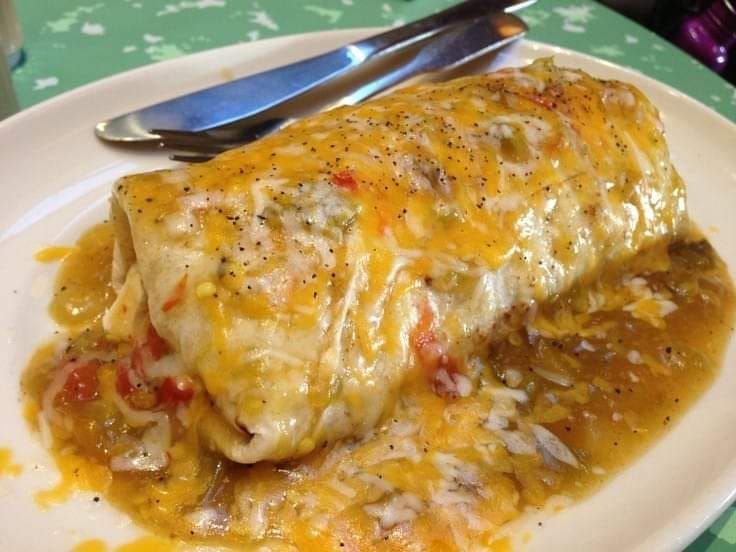 an enchilada on a white plate with a fork and knife next to it