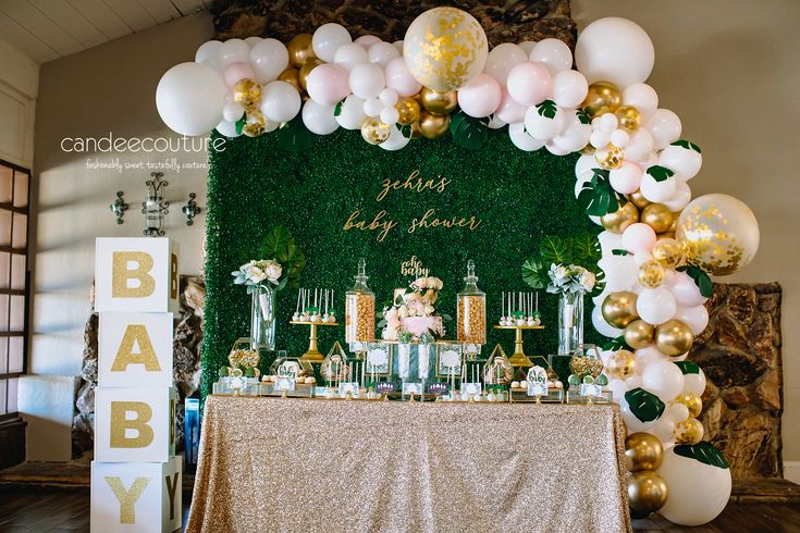 a table topped with cakes and desserts next to a wall covered in greenery