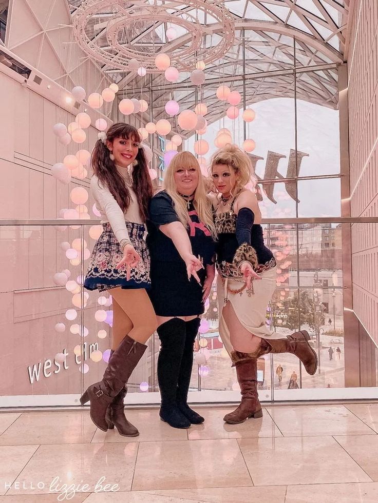 three women posing for a photo in front of a glass wall with balloons hanging from it