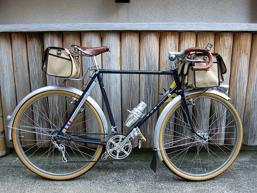 a bike parked next to a wooden fence with a bag on the front rack and seat